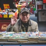 An elderly vendor selling books at a vibrant Tianjin street market.